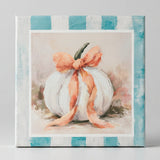 A square decorative canvas print featuring a white pumpkin with a peach-pink bow, styled on a rustic wooden surface next to a dark ceramic vase.